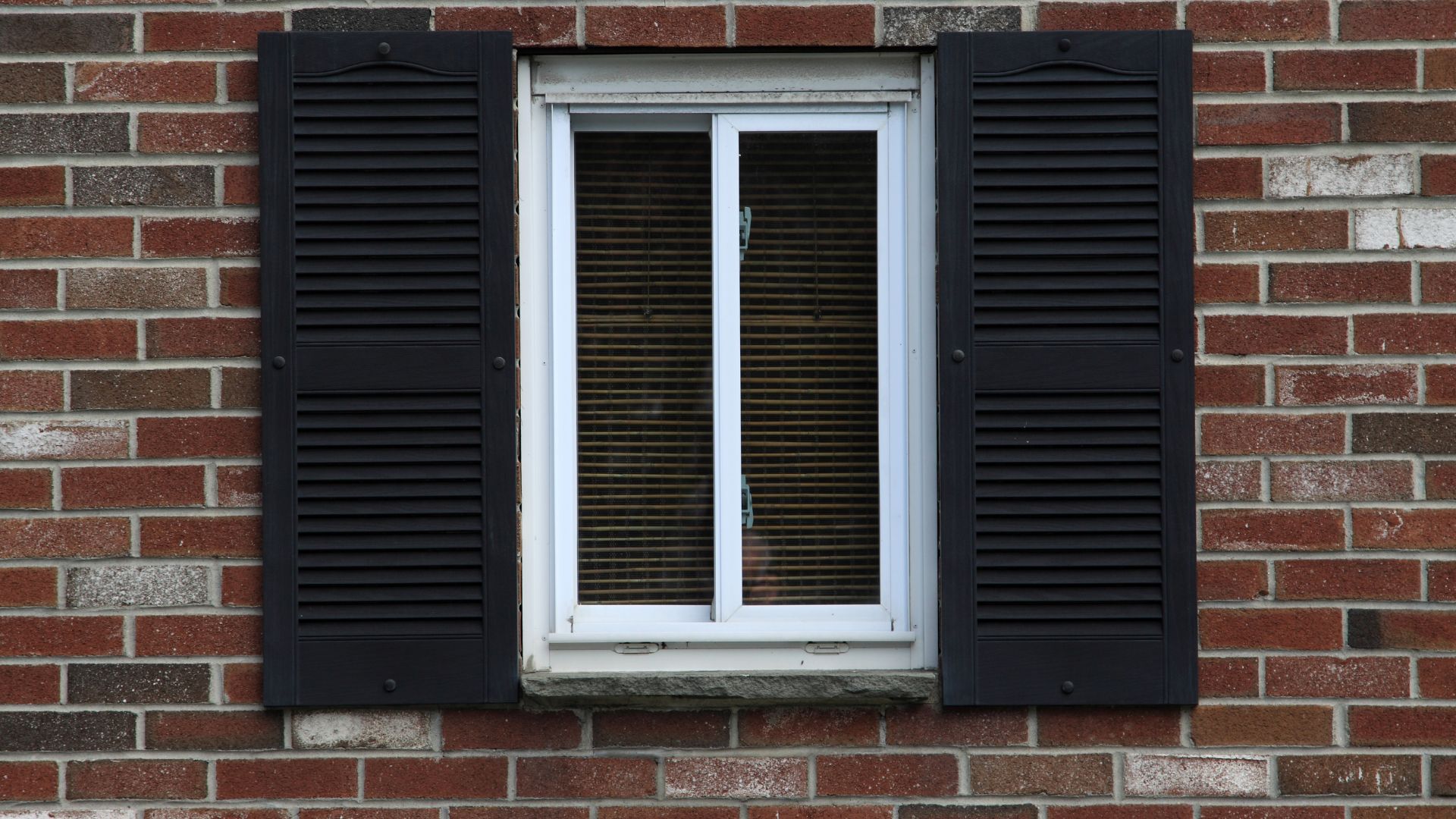 A brick wall with black shutters and a white window